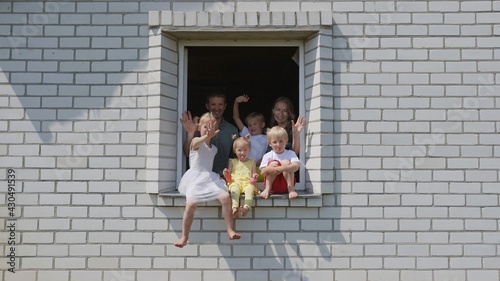 The concept of a large family. A friendly family waves their hands from the window of their home.
