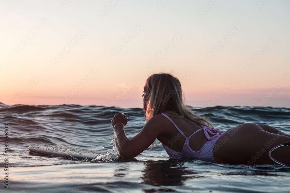 Portrait from the water of surfer girl with beautiful body on surfboard in the ocean at sunset time Portrait from the water of surfer girl with beautiful body on surfboard in the ocean at sunset time