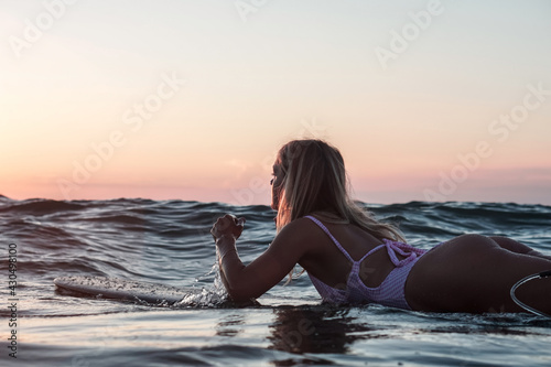 Portrait from the water of surfer girl with beautiful body on surfboard in the ocean at sunset time