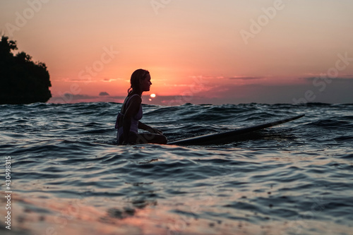 Portrait from the water of surfer girl with beautiful body on surfboard in the ocean at sunset time i