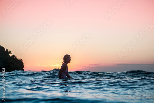 Portrait from the water of surfer girl with beautiful body on surfboard in the ocean at sunset time in Bali