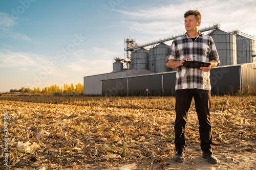 Fotografia Man farmer or engineer standing by the agricultural silos with tablet in his han