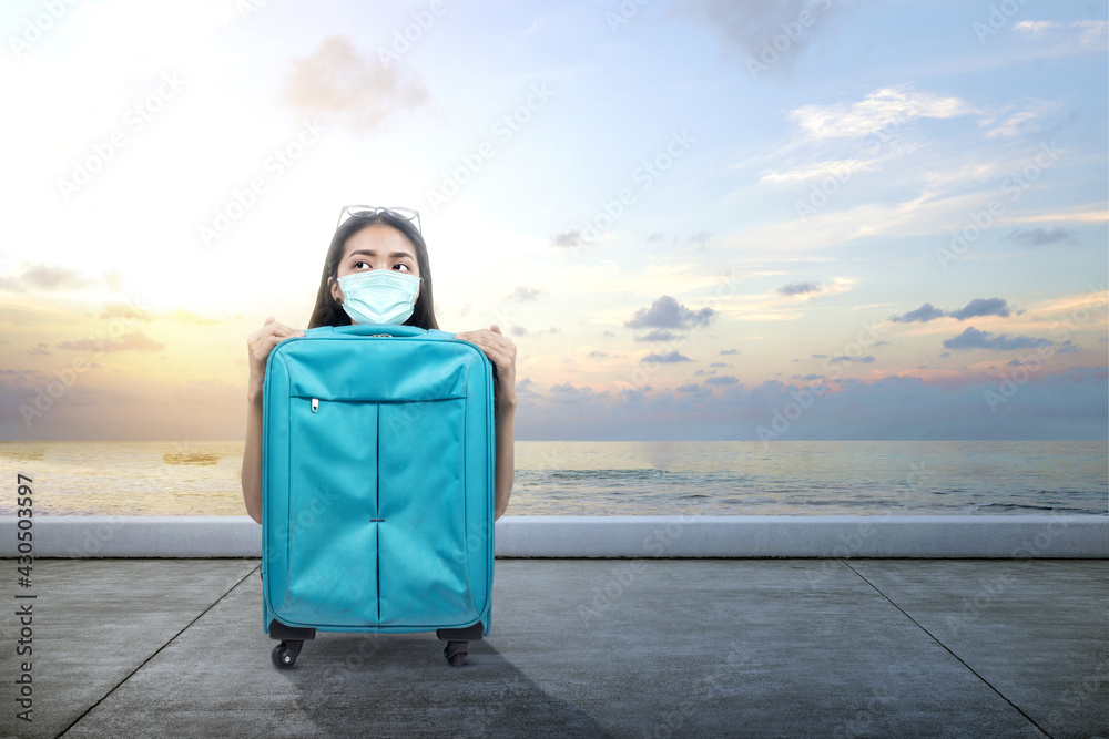 Fototapeta premium Asian woman with a face mask with a suitcase on the dock