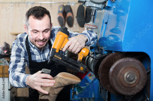 Positive male worker repairing shoes in repair workshop