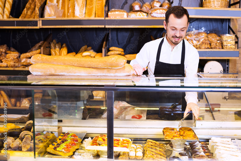 Positive young seller offering fresh tasty bun in bakery