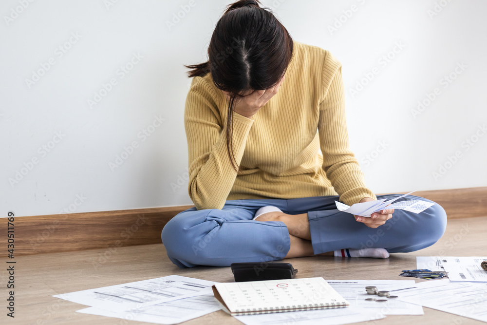 Fototapeta premium Front view owe asian woman, female sitting on floor home, stressed and confused by calculate expense from invoice or bill, have no money to pay, mortgage or loan. Debt, bankruptcy or bankrupt concept.