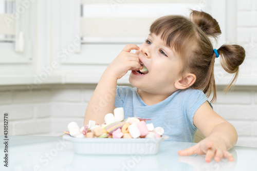 cute European female child smiling, happily eating candy, with appetite. sugar abuse, unhealthy sweet food concept, child candy addiction and child dental care