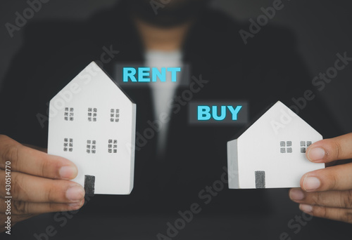Businessman hand holding white home with text RENT and BUY for customer choice.