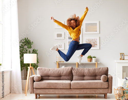 Canvas-taulu Happy african american teen girl jumping on sofa while having fun on weekend at