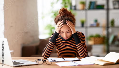 Stressed young afro american female feeling tired while working remotely or studying online at home photo