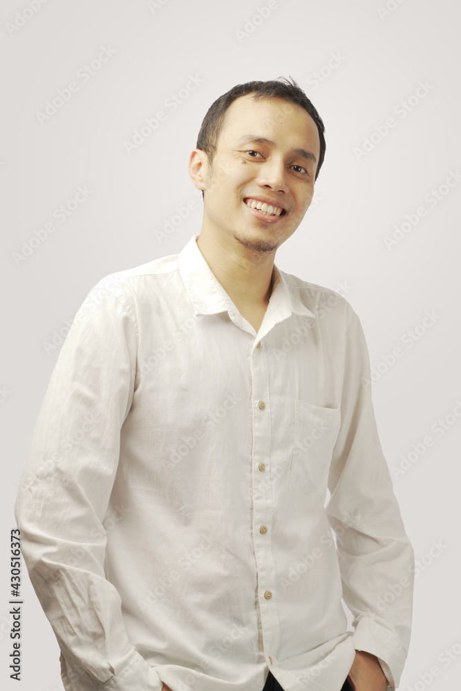 Smiling young man in white t-shirt looking at camera while standing against gray background. Smiling young man in white t-shirt looking at camera while standing against gray background.