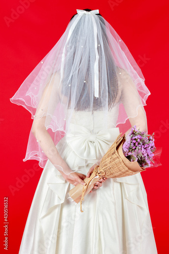 The bride in a white lace  wedding dress holding a purple bouquet standing back and look at the studio in red background. Concept loce happy lovely. photo