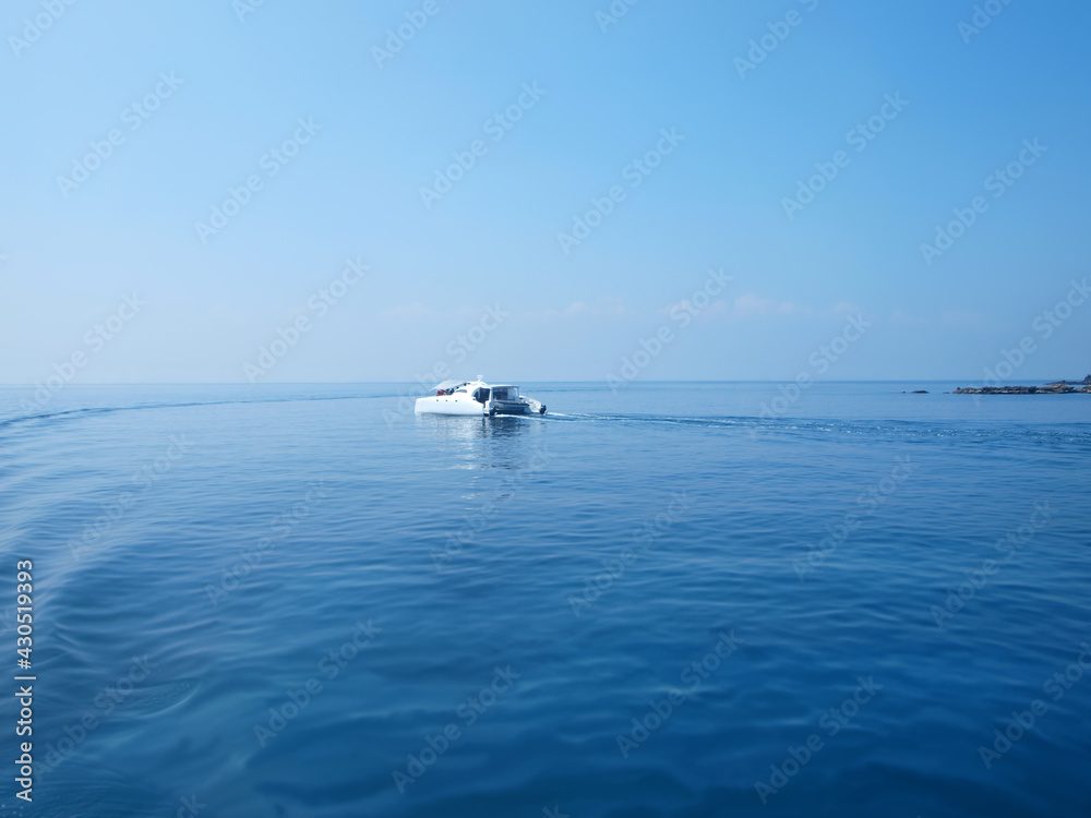 Beautiful view of sea and yacht. Scene of motor yacht in the sea. Rocks on a distance. Horizon line. Ripple and wake trace on the surface of water. Pleasure tourist boat, sea travel, touristic service
