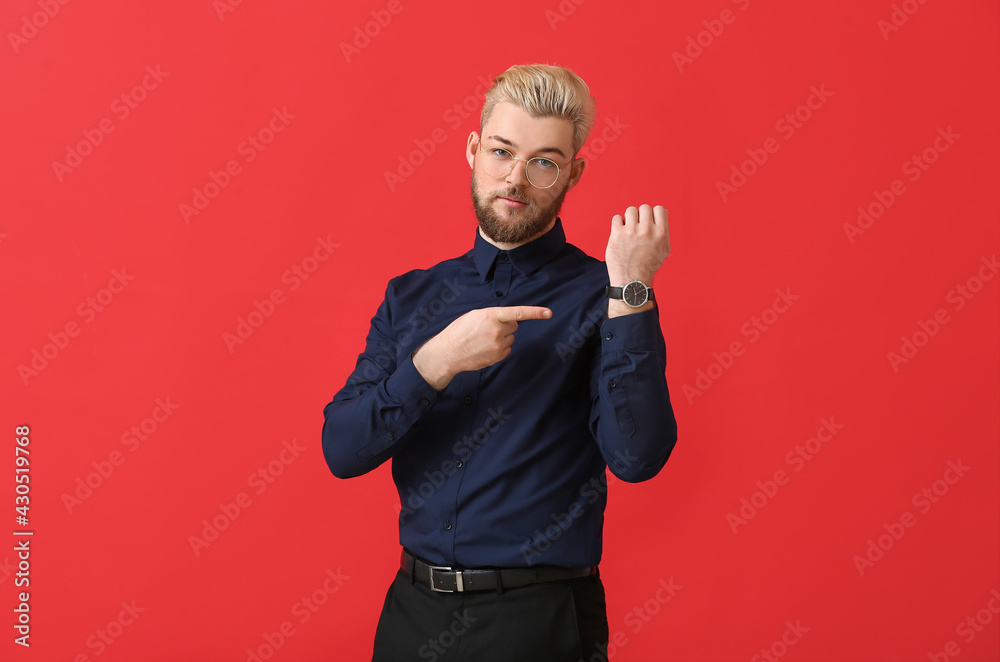 Young man pointing at wristwatch on color background Young man pointing at wristwatch on color background