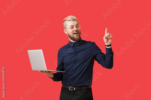 Young man with laptop pointing at something on color background