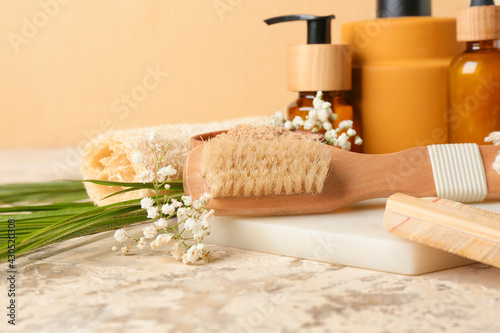 Composition with massage brush, bath supplies and flowers on color background