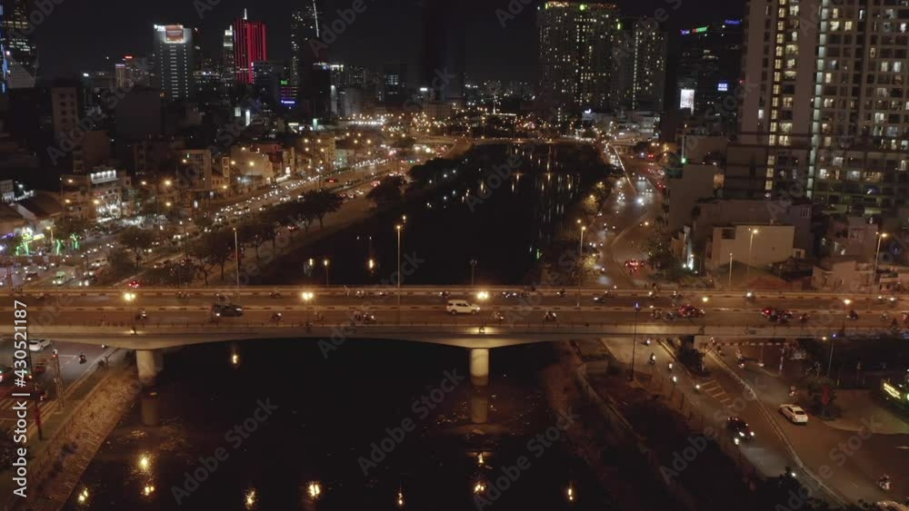 aerial tripod view across busy traffic bridge at night. The bridge crosses a river reflecting lights of the city skyline