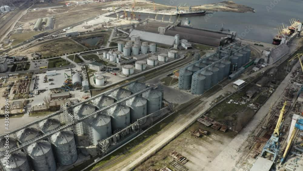 Grain elevator and silos near the river aerial view. Aerial view large waterfront grain storage facility with concrete silos and train yard. Grain elevator and silos near the river aerial view. Aerial view large waterfront grain storage facility with concrete silos and train yard.
