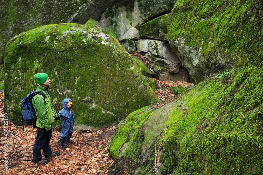 Father and son on haking trail near huge stones covered by green moss. Active family outdoor. Travel adventure with child.