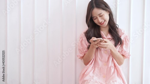 Cute woman use phone for chat or shop and sitting near white wall