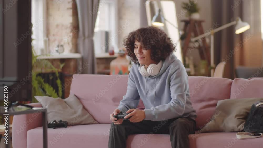 Mixed race teenage boy sitting on sofa at home, smiling and playing video game on console Mixed race teenage boy sitting on sofa at home, smiling and playing video game on console