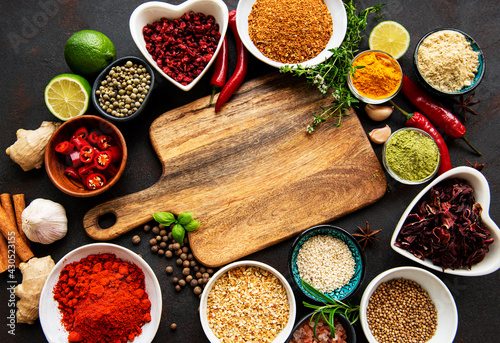 Various spices in a bowls and empty cutting board on black concrete background. Top view copy space.