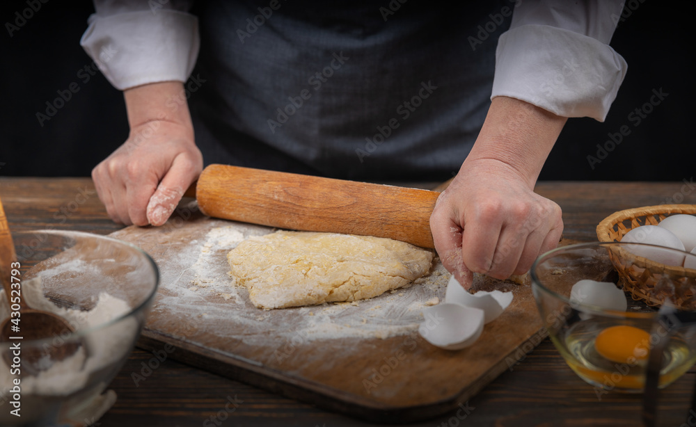 Women's hands, flour and dough. A woman in an apron cooking dough for homemade baking, a rustic home cozy atmosphere, a dark background with unusual lighting. Women's hands, flour and dough. A woman in an apron cooking dough for homemade baking, a rustic home cozy atmosphere, a dark background with unusual lighting.