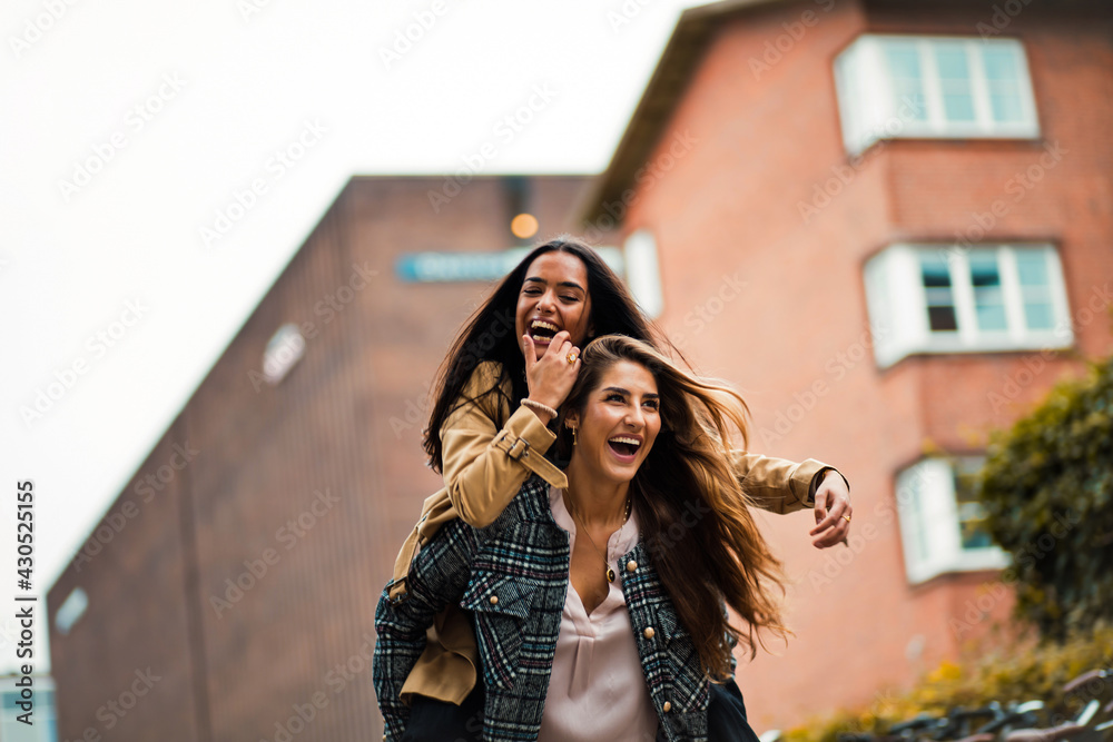 Two women having fun outside. Girl carrying friend on piggyback.