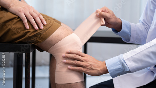 Medical concept a male doctor putting a bandage on knee's male patient after his accident