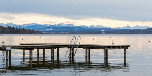 Empty pier at Ammersee lake. Alps in the distance at the horizon. Panorama format.