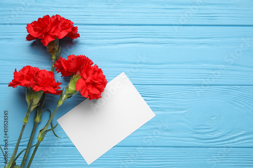 Fresh carnation flowers with empty paper sheet on color wooden background photo