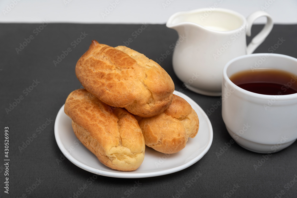 Eclairs and tea with milk. Traditional French eclairs. Profiteroles on white saucer.