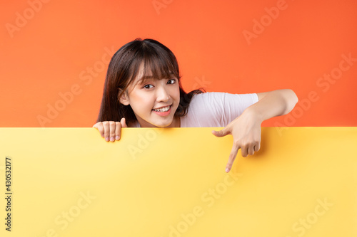 Young Asian girl pointing her finger down on yellow and orange background