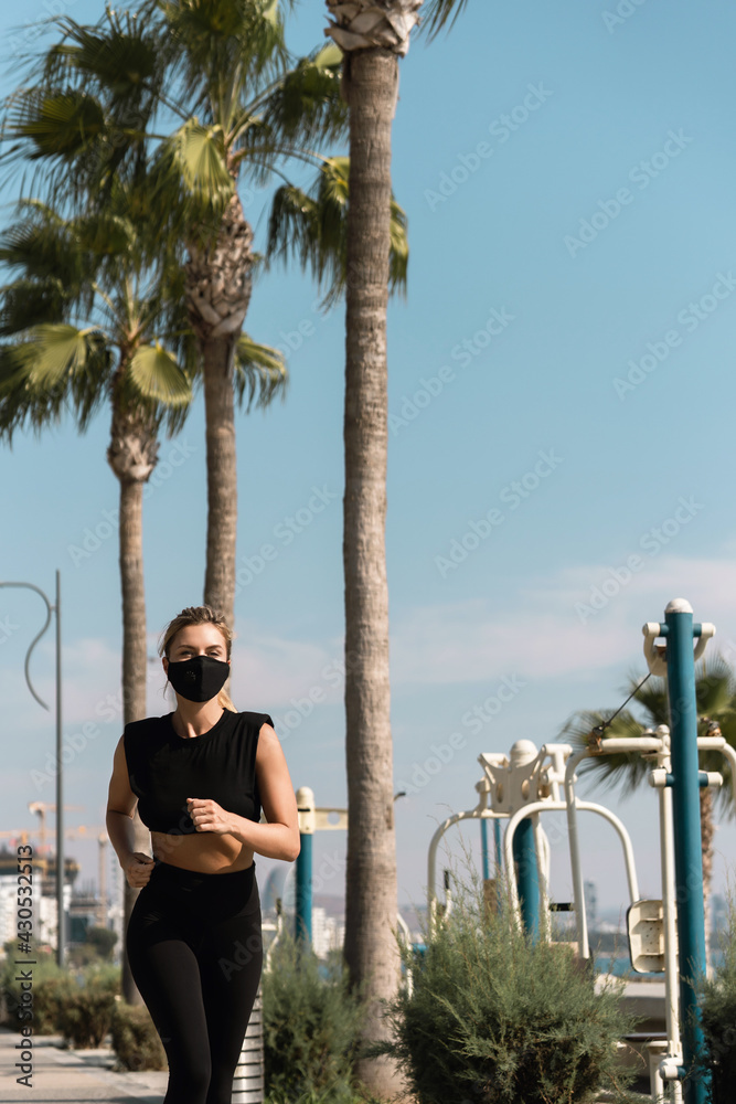 Fototapeta premium Athletic woman wearing face mask is running during her summer jogging workout