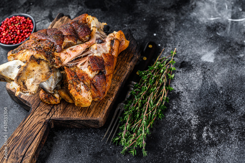 Roasted pork knuckle eisbein on a wooden board with herbs. Black background. Top view. Copy space