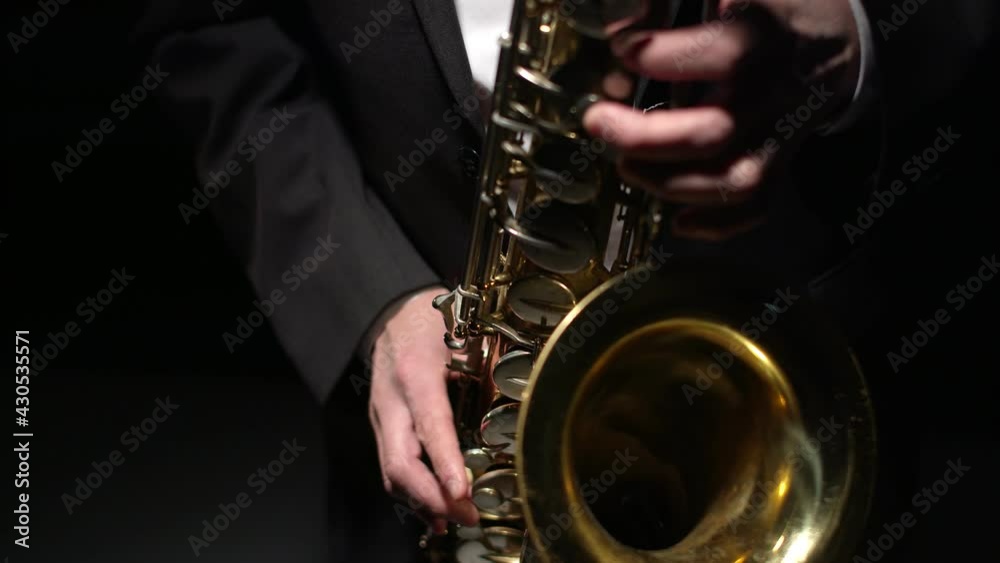 Musician in formal suit plays shiny saxophone with hands in the studio