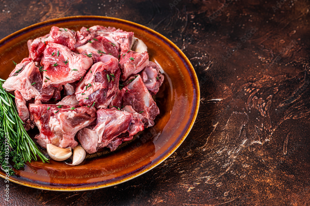 Raw mutton meat diced for goulash or stew with bone on a rustic plate. Dark background. Top view. Copy space