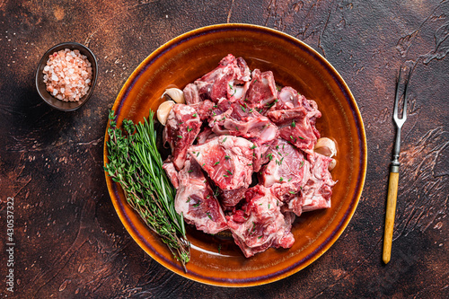 Raw mutton meat diced for goulash or stew with bone on a rustic plate. Dark background. Top view