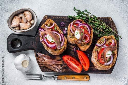 Toasts with olive oil, herbs, tomatoes and spicy anchovy fillets. White background. Top view