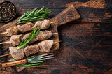 Pork meat Shish kebab on skewers with herbs  on a wooden board. Dark wooden background. Top view. Copy space