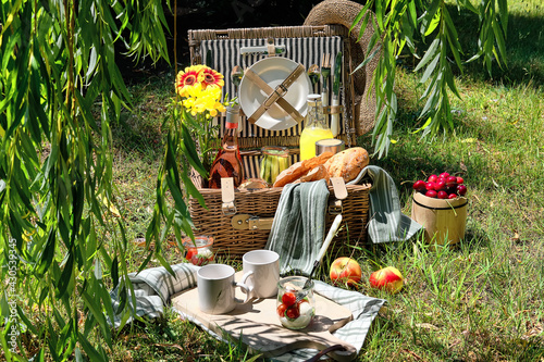 Vintage picnic basket, hamper with baguette and lemonade outdoors on a grass with cheese, mozzarella, tomatoes, cherries, vine. Eco friendly picnic al fresco. photo