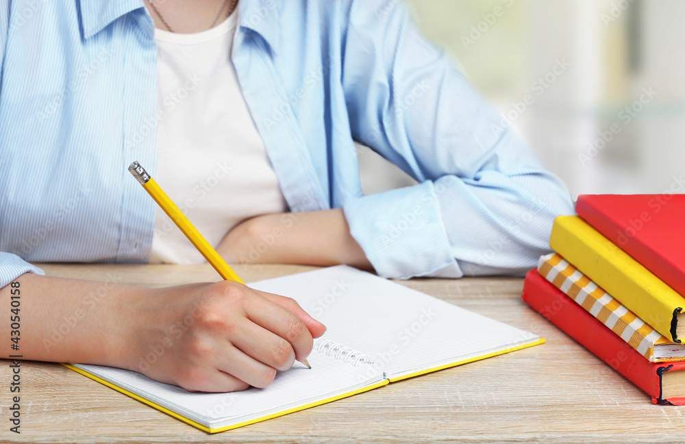 Child girl writing in copybook with pencil. Pupil at the desk, stack of books. School homework.Studing process. Education concept. Child girl writing in copybook with pencil. Pupil at the desk, stack of books. School homework.Studing process. Education concept.