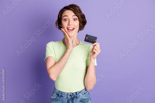 Portrait of lovely cheerful amazed girl holding in hands bank card isolated over violet color background
