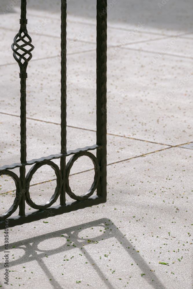 Sunlight and shadow on surface of the old vintage black metal gate fence with many green pollen falling on gravel stone floor in vertical frame