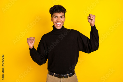 Photo of lucky funny dark skin man wear black jumper rising fists isolated yellow color background