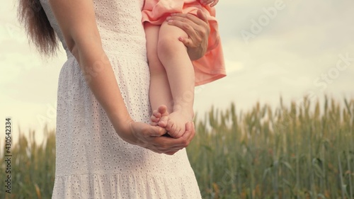 Family, baby and mommy are walking in park in summer. Little daughter sits barefoot in her mothers arms, mother walks with child in field in spring. Kid, mom walk travel together outdoor recreation