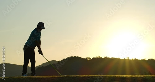 Slow Motion Golf Swing Drive Shot. Silhouette Asian male golfer enjoying vacation luxury resort using driver to tee off golf course fairway over sunset background. photo