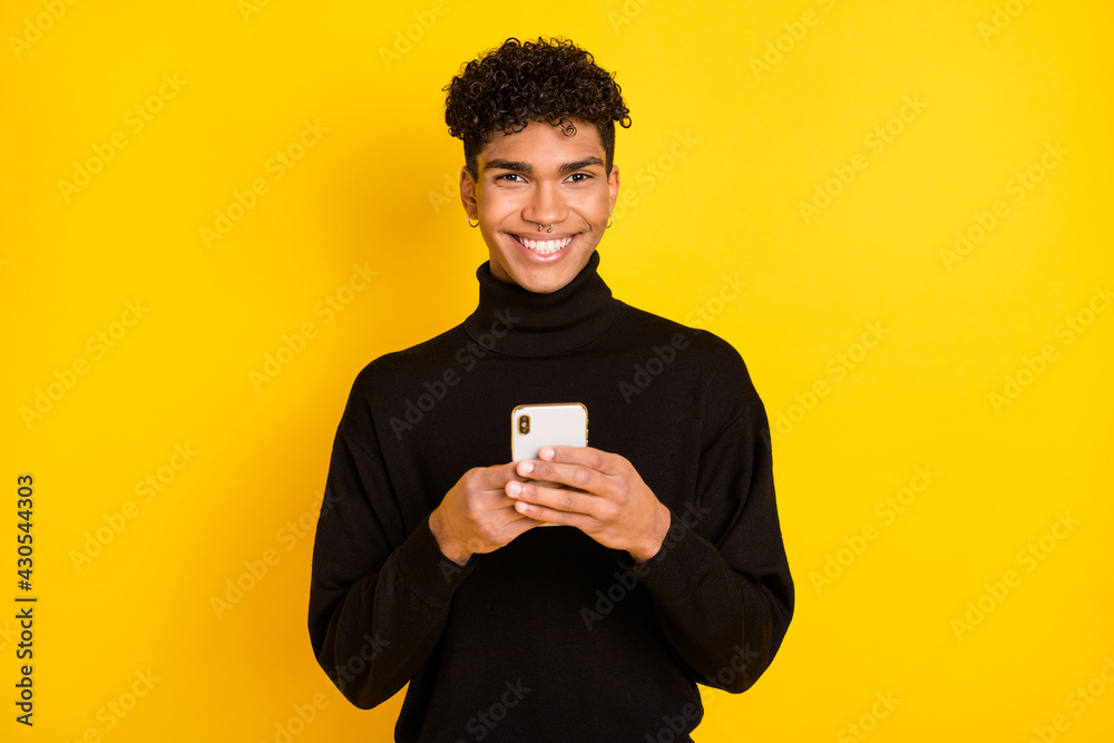 Photo of cute sweet dark skin guy dressed black turtleneck typing modern device isolated yellow color background Photo of cute sweet dark skin guy dressed black turtleneck typing modern device isolated yellow color background