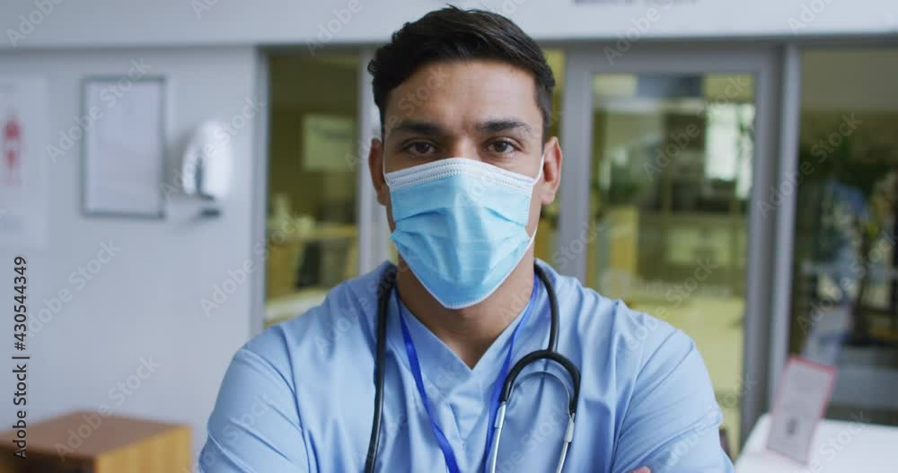 Portrait of mixed race male doctor wearing scrubs and face mask standing in hospital Portrait of mixed race male doctor wearing scrubs and face mask standing in hospital