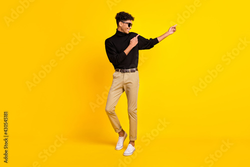 Photo of cool attractive dark skin guy dressed black jumper glasses dancing pointing empty space isolated yellow color background